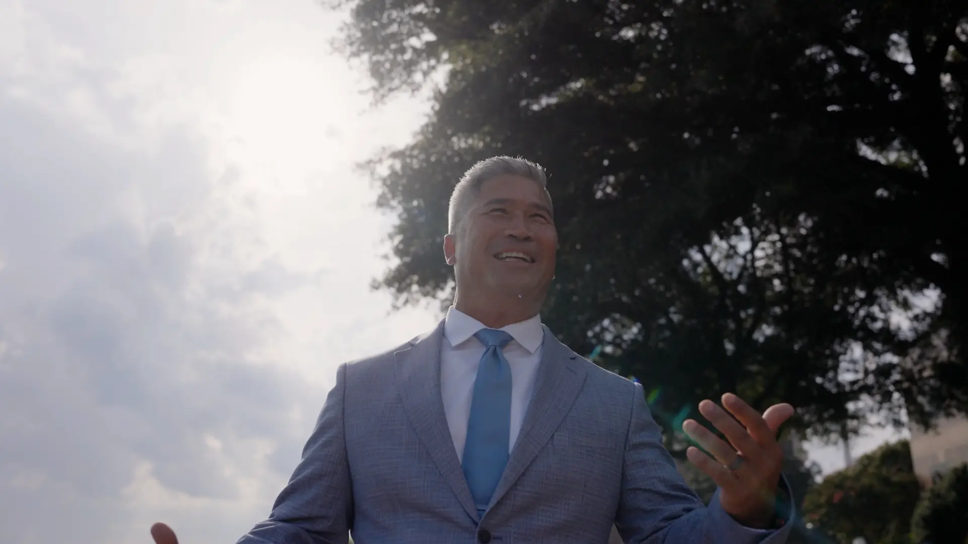[CONFIRM] Dr Walt Whitley smiling outdoors against a bright sky and trees.