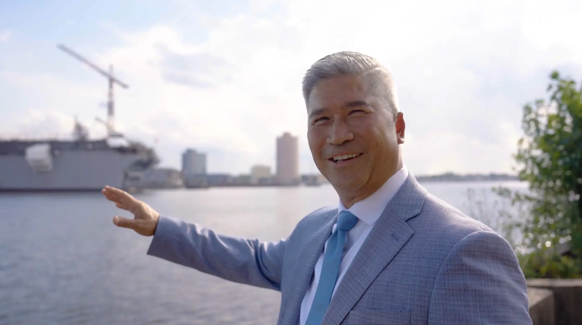 [CONFIRM] Dr Walt Whitley smiling and gesturing on the waterfront with the city behind him.